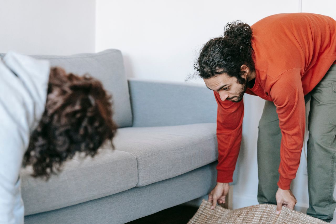 hero-img A couple tidying up their living room, organizing furniture and rugs with teamwork.